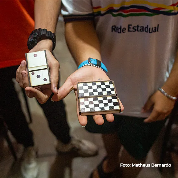 Mãos exibem peças de madeira em padrão xadrez