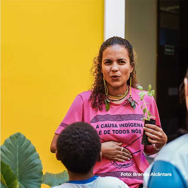 Pesquisadora fala em evento, com a faixa "A causa indígena é de todos nós"